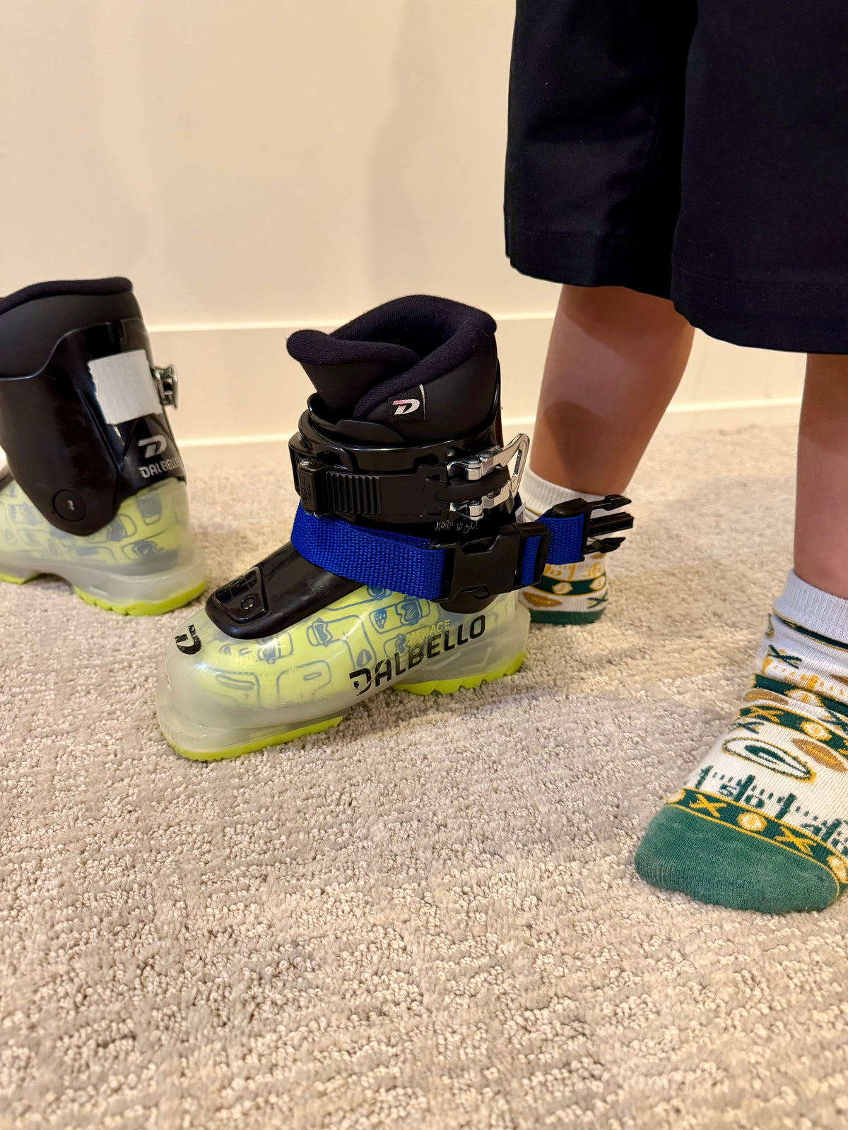 Two kids' ski boots set up on the living room carpet, ready for boot work practice.